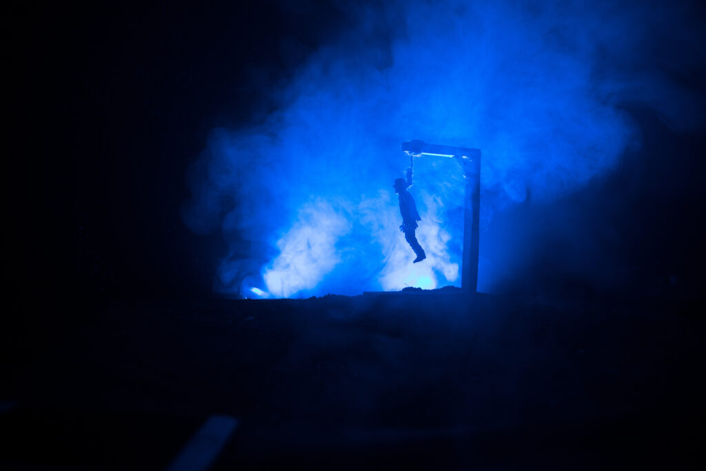 horror view silhouette of hanged man on scaffold at night with fog and toned light on background. execution (or suicide) decoration.